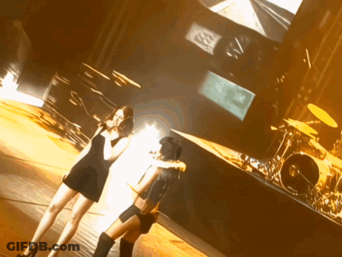 Two Women On Stage With Drum Set And SD Screen GIF