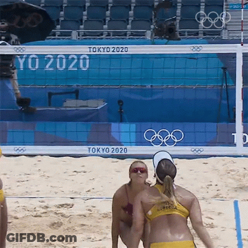 Two Women Playing Beach Volleyball In Front Of A Tokyo 2020 Sign GIF
