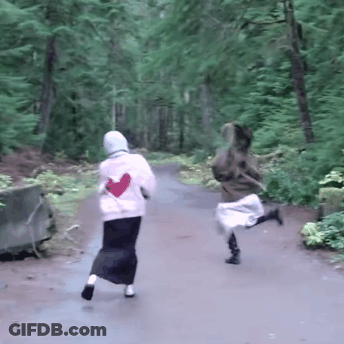 Two Women Running Down Path In Woods One With Heart Shirt GIF