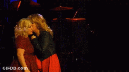 Two Women Singing In Front Of A Drum Set In A Dark Room GIF