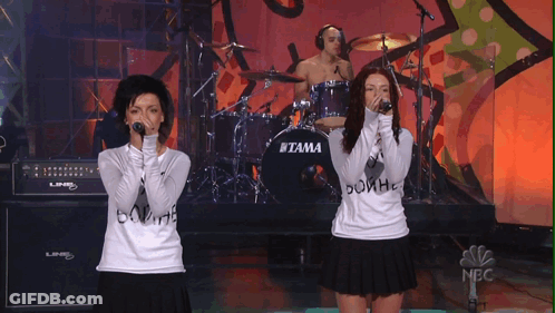 Two Women Singing In Front Of Tama Drum Set GIF