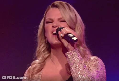 Two Women Singing Into Microphones On A Stage In Front Of A Band GIF