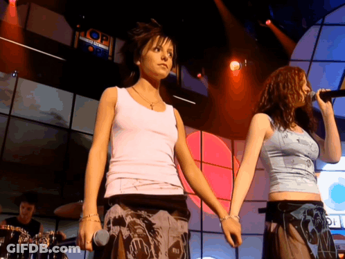 Two Women Singing Into Microphones On Stage GIF