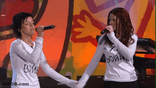 Two Women Singing Into Microphones, One Wearing NBC Shirt GIF