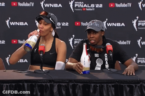 Two Women Sit At A Table In Front Of A Youtube TV Sign GIF