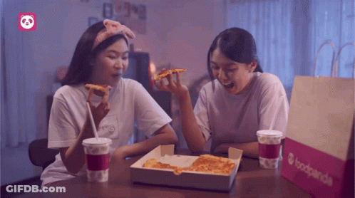 Two Women Sit At A Table With A Box Of Pizza And A Bag That Says Foodpanda GIF