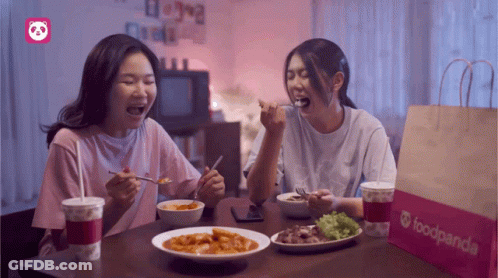 Two Women Sit At A Table With Food And A Bag That Says Foodpanda On It GIF