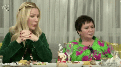 Two Women Sit At A Table With Plates Of Food And A Sign That Says Seda Sayan Ile On It GIF