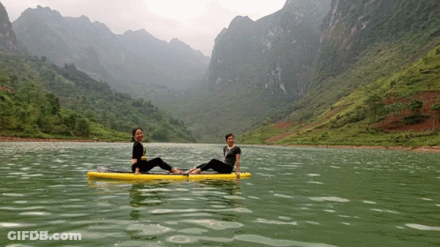 Two Women Sit On A Paddle Board In A Lake GIF