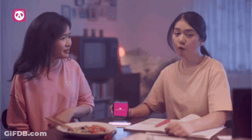 Two Women Sitting At A Table With A Phone That Says ' Panda ' On It GIF