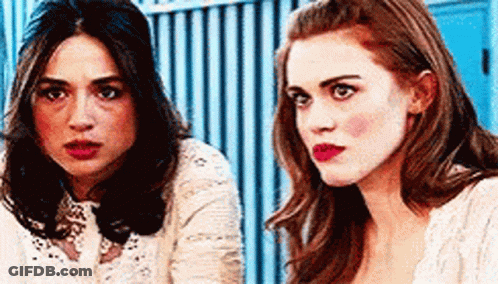 Two Women Sitting Next To Each Other In Front Of Blue Fence GIF