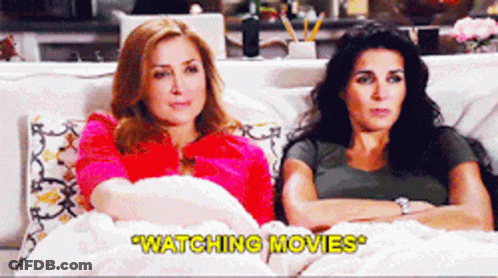 Two Women Sitting On A Couch Watching Movies With The Caption " Watching Movies " GIF