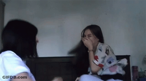 Two Women Sitting On Bed Laughing And Covering Mouths GIF