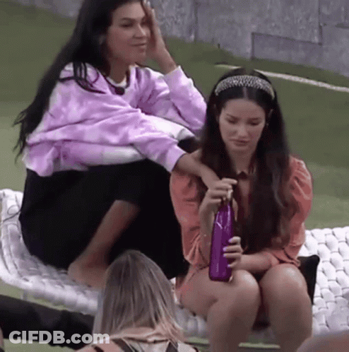 Two Women Sitting On Blanket One Holding Purple Bottle GIF