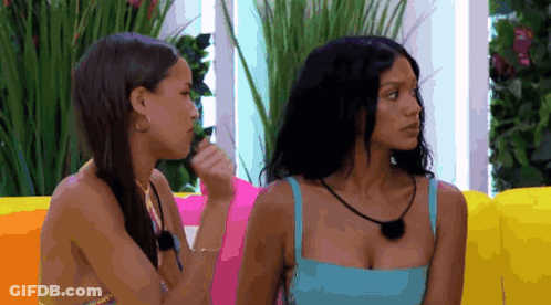 Two Women Sitting On Colorful Couch, One In Blue Top GIF