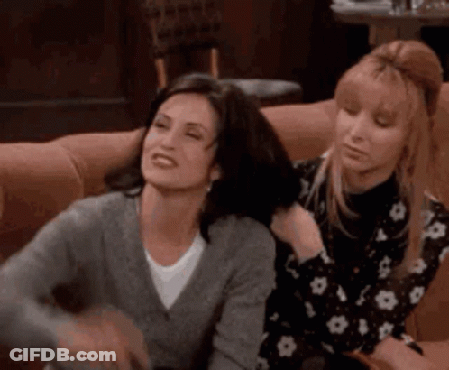 Two Women Sitting On Couch, One Brushing Other's Hair GIF