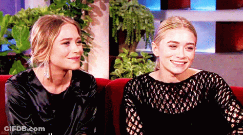 Two Women Sitting On Red Couch GIF