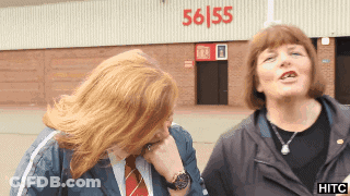 Two Women Standing In Front Of A Building With 56/55 On It GIF