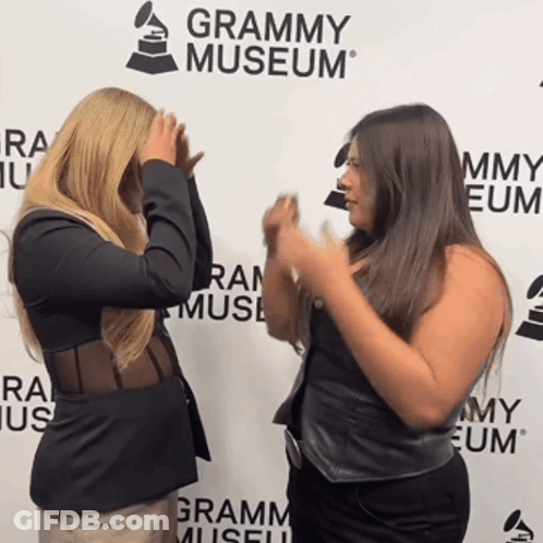 Two Women Standing In Front Of A Grammy Museum Sign GIF