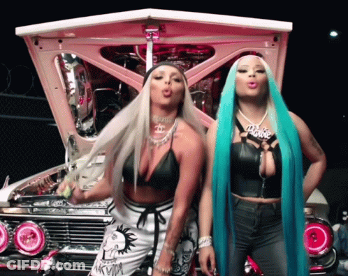 Two Women Standing In Front Of A Pink Car And One Has A Barbie Necklace GIF