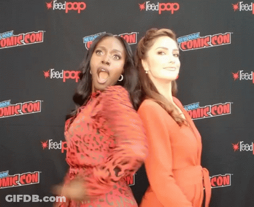 Two Women Standing In Front Of A Wall That Says Comic Con On It GIF