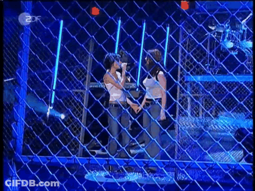 Two Women Standing In Front Of Chain Link Fence GIF