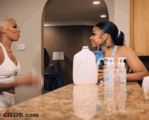 Two Women Standing In Front Of Counter With Gallon Of Milk GIF