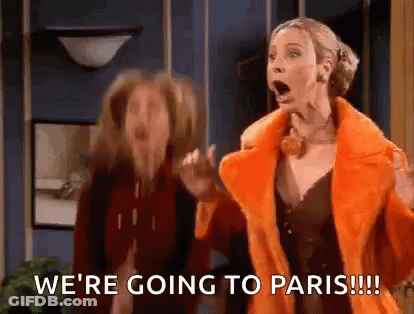 Two Women Standing In Room One In Orange Coat GIF