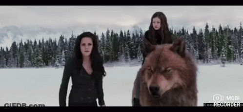 Two Women Standing Next To A Wolf In The Snow With A Mobi Logo On The Bottom Left GIF