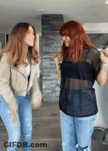 Two Women Standing Next To Each Other Dancing In Front Of A Stone Wall GIF