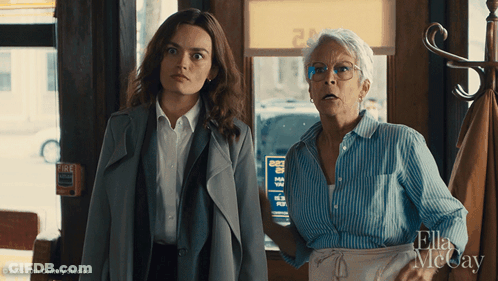 Two Women Standing Next To Each Other In Front Of A Sign That Says " Fire " GIF