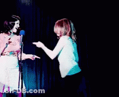 Two Women Standing Next To Each Other On A Stage GIF