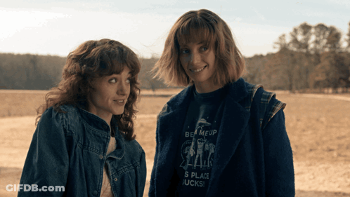 Two Women Standing Next To Each Other One Wearing A Shirt That Says Be Me Up GIF