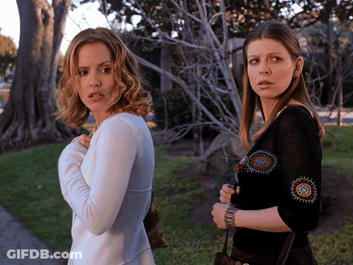 Two Women Standing Next To Each Other With One Wearing A Black Top GIF