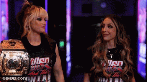 Two Women Standing Next To Each Other With One Wearing A T-Shirt That Says ' Smack Down ' On It GIF