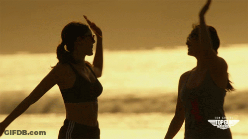 Two Women Standing On A Beach With The Words Top Gun America On The Bottom Right GIF