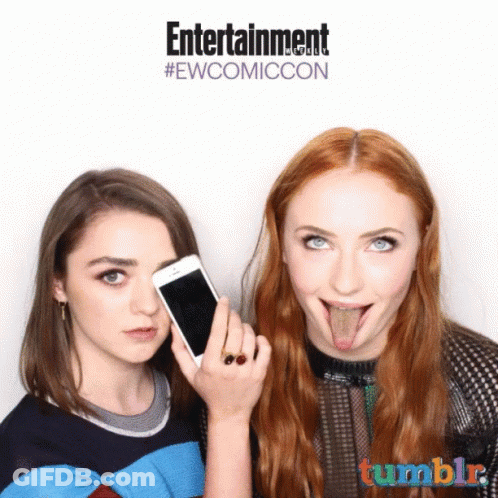 Two Women Sticking Their Tongues Out In Front Of A Sign That Says Entertainment #Ewcomiccon GIF