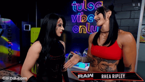 Two Women Talking In Front Of A Sign That Says Tulsa Vibe Only GIF
