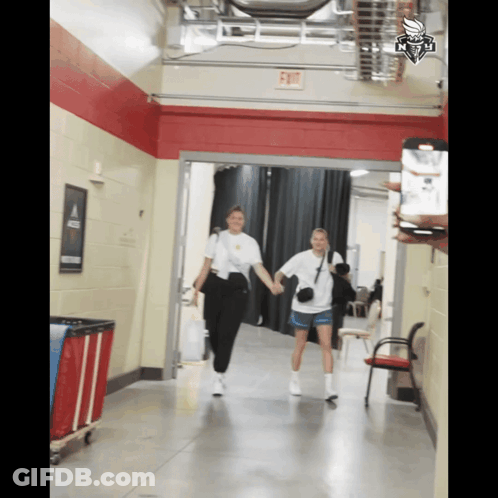 Two Women Walking Down Hallway With Exit Sign GIF