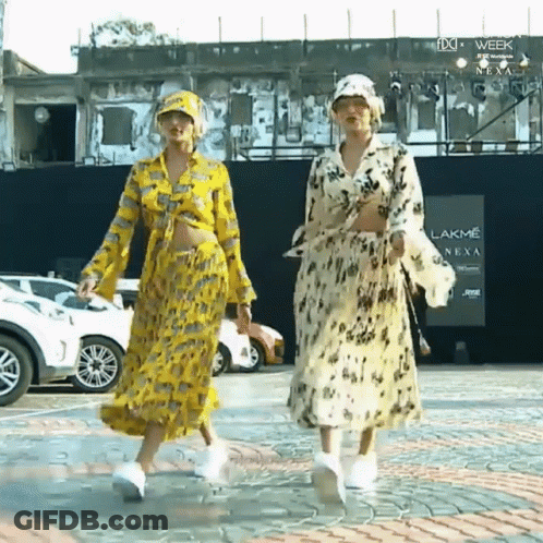 Two Women Walking In Front Of Lakme Sign GIF