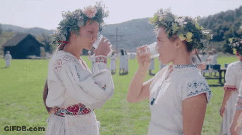 Two Women Wearing Floral Wreaths Drinking Water GIF