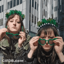 Two Women Wearing Green Glasses And A Green Crown GIF