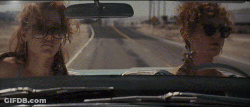 Two Women Wearing Sunglasses Are Driving Down A Road In A Car GIF