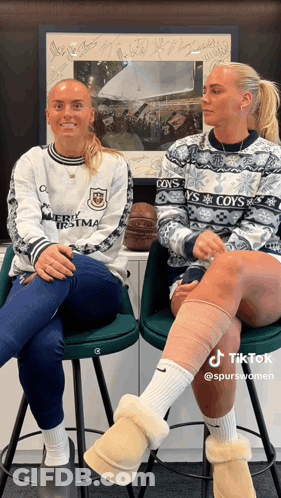 Two Women Wearing Sweaters That Say Coy 'S Are Sitting On Stools GIF