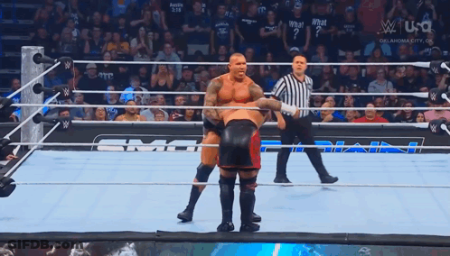 Two Wrestlers Are In A Wrestling Ring With A Referee Standing Behind Them GIF