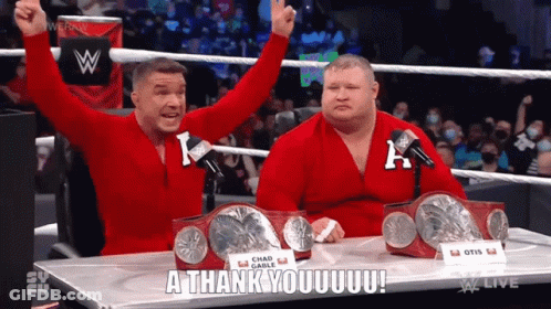 Two Wrestlers Are Sitting At A Table With Their Arms In The Air And One Of Them Is Saying A Thank You GIF