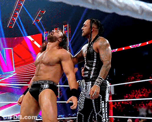 Two Wrestlers Are Standing In A Ring And One Of Them Is Wearing A Black And White Outfit With The Word WWE On It GIF