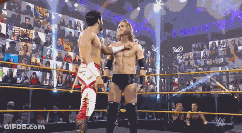 Two Wrestlers Are Standing In A Wrestling Ring With A Crowd Behind Them And The Letters W On The Wall GIF