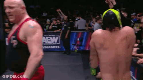 Two Wrestlers Are Standing In Front Of A Aew Dynamite Sign GIF