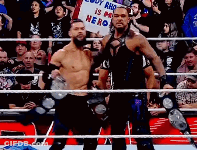 Two Wrestlers Are Standing Next To Each Other In A Wrestling Ring Holding A Sign . GIF